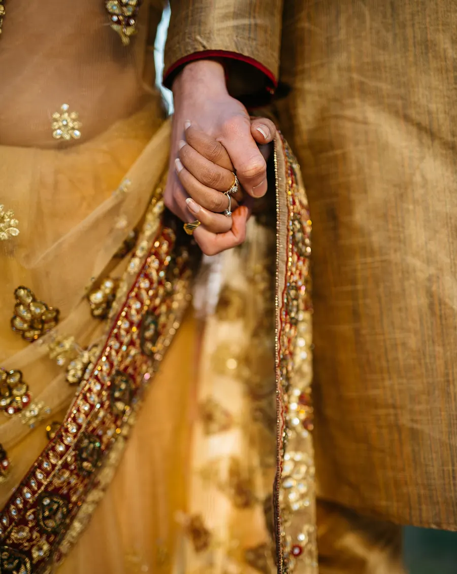 An Indian couple in gold traditional wedding attire holding hands