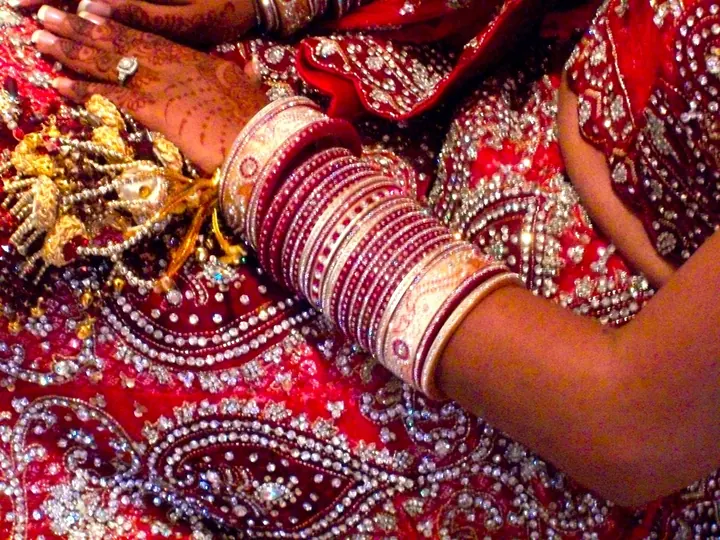 Close-up of a bride's red embroidered lehenga, bangles and kalire
