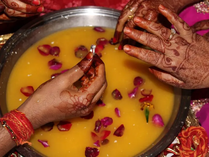 A newly married couple playing the traditional ring-finding game in a bowl of milk and rose petals